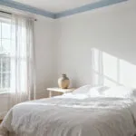 A sophisticated bedroom interior in shades of white, showcasing how various white hues and textures – from warm-toned walls to cool linen and ceramic – interplay under soft natural light, creating a psychologically resonant and serene ambiance.