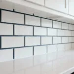 White subway tile kitchen backsplash with dark gray grout and white shaker cabinets.