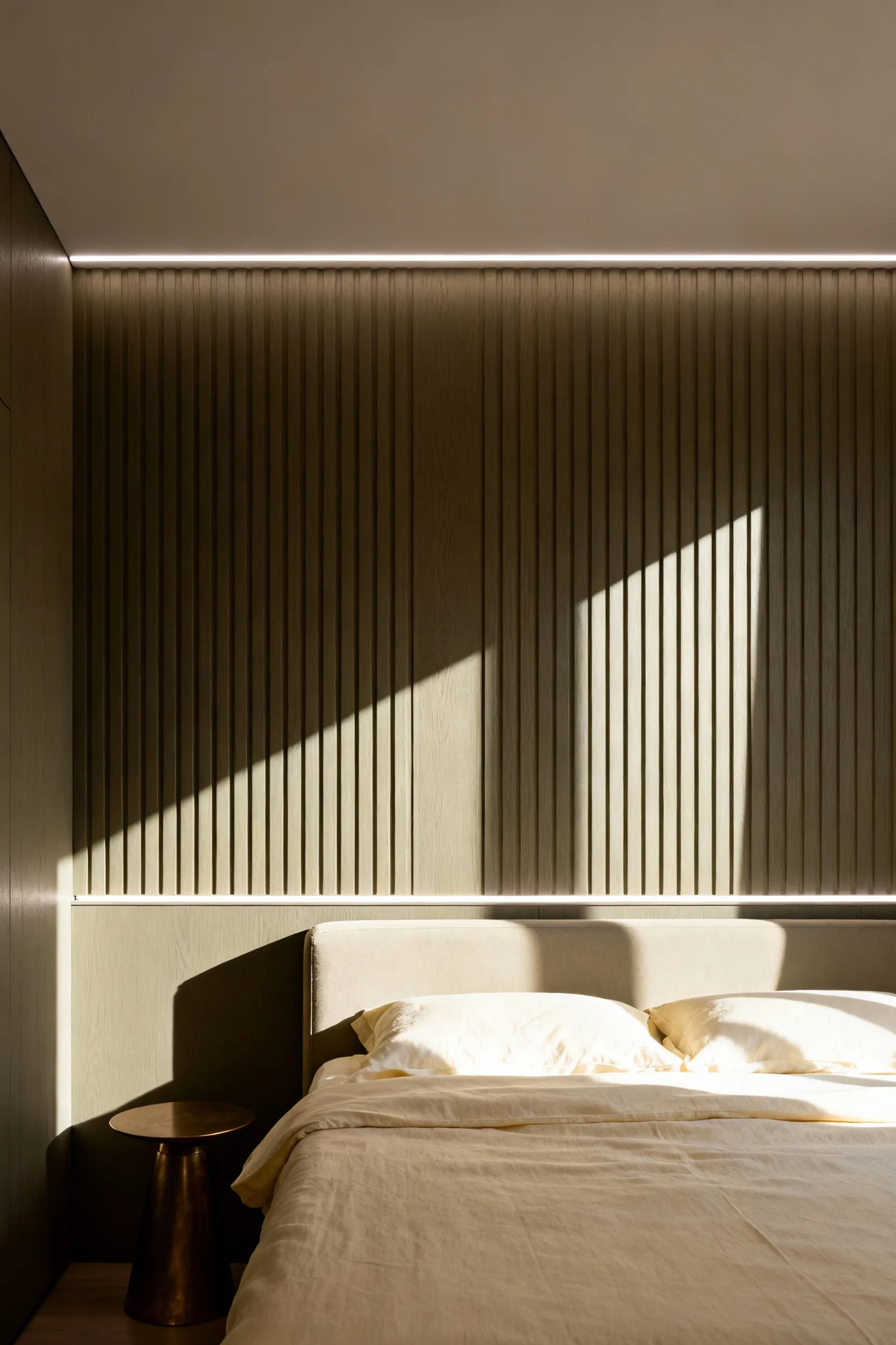 A sophisticated bedroom featuring a textured, vertically fluted accent wall dramatically illuminated by linear LED wall grazing lights, emphasizing the deep shadows and highlights of the texture.