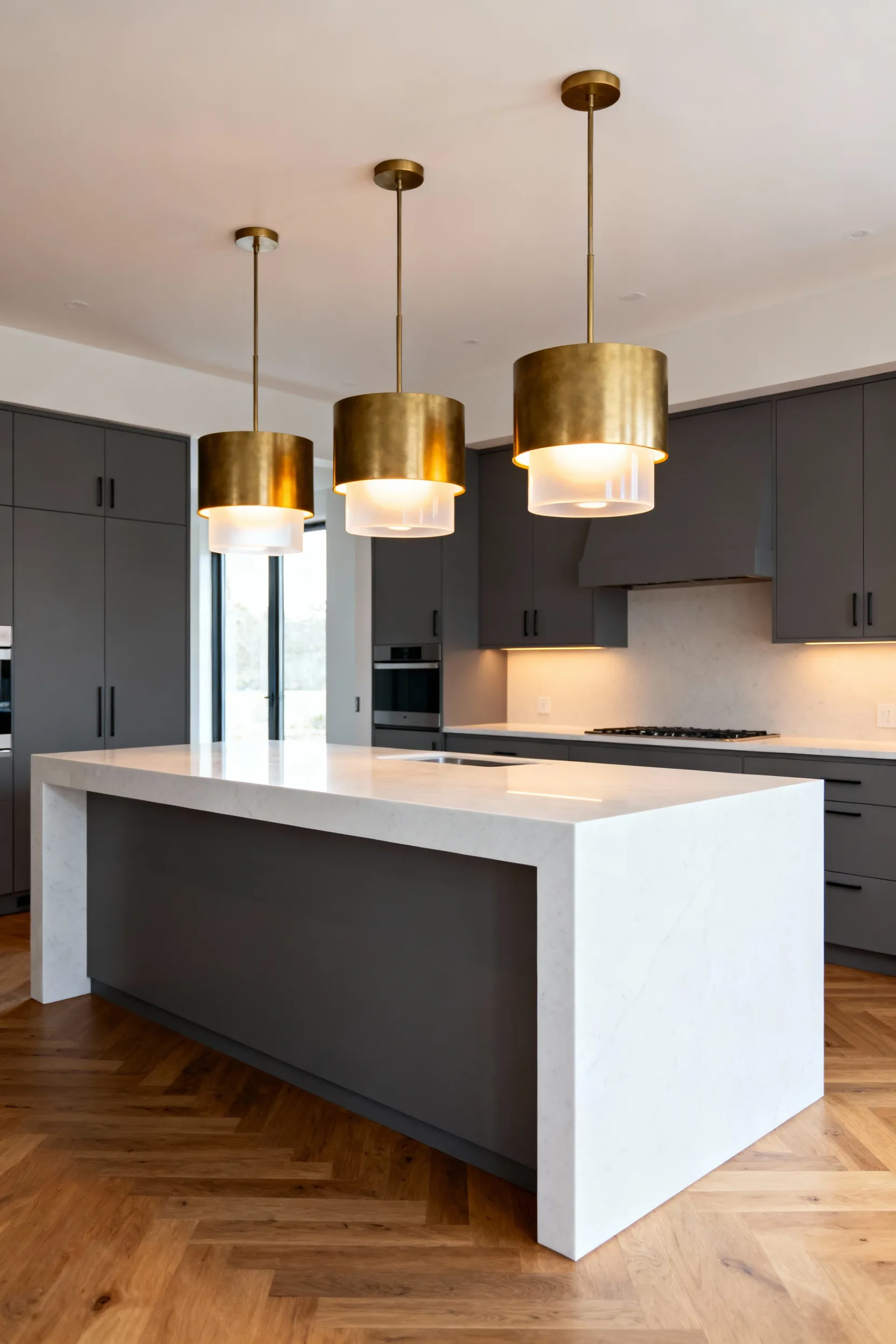 Three perfectly scaled brass drum pendant lights hanging above a long white quartz kitchen island, demonstrating ideal visual weight.