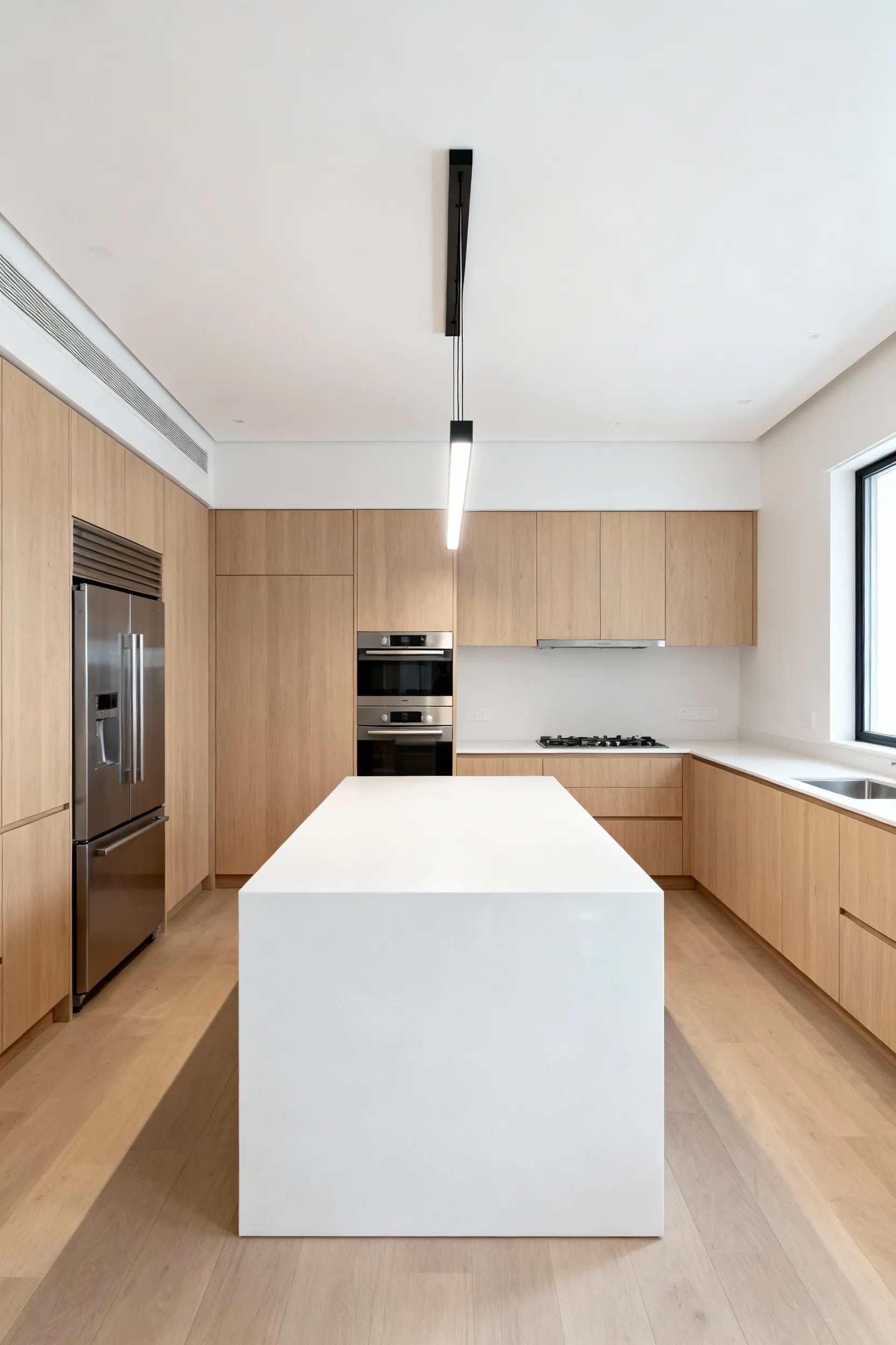 A bright, modern kitchen with an eight-foot ceiling featuring a long white quartz island and light wood cabinetry, illuminated by a sleek, linear LED light bar that minimizes vertical drop.