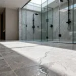 Seamless luxury bathroom flooring made of high-density porcelain tiles replicating the organic grain of honed taupe limestone in a walk-in shower setting.