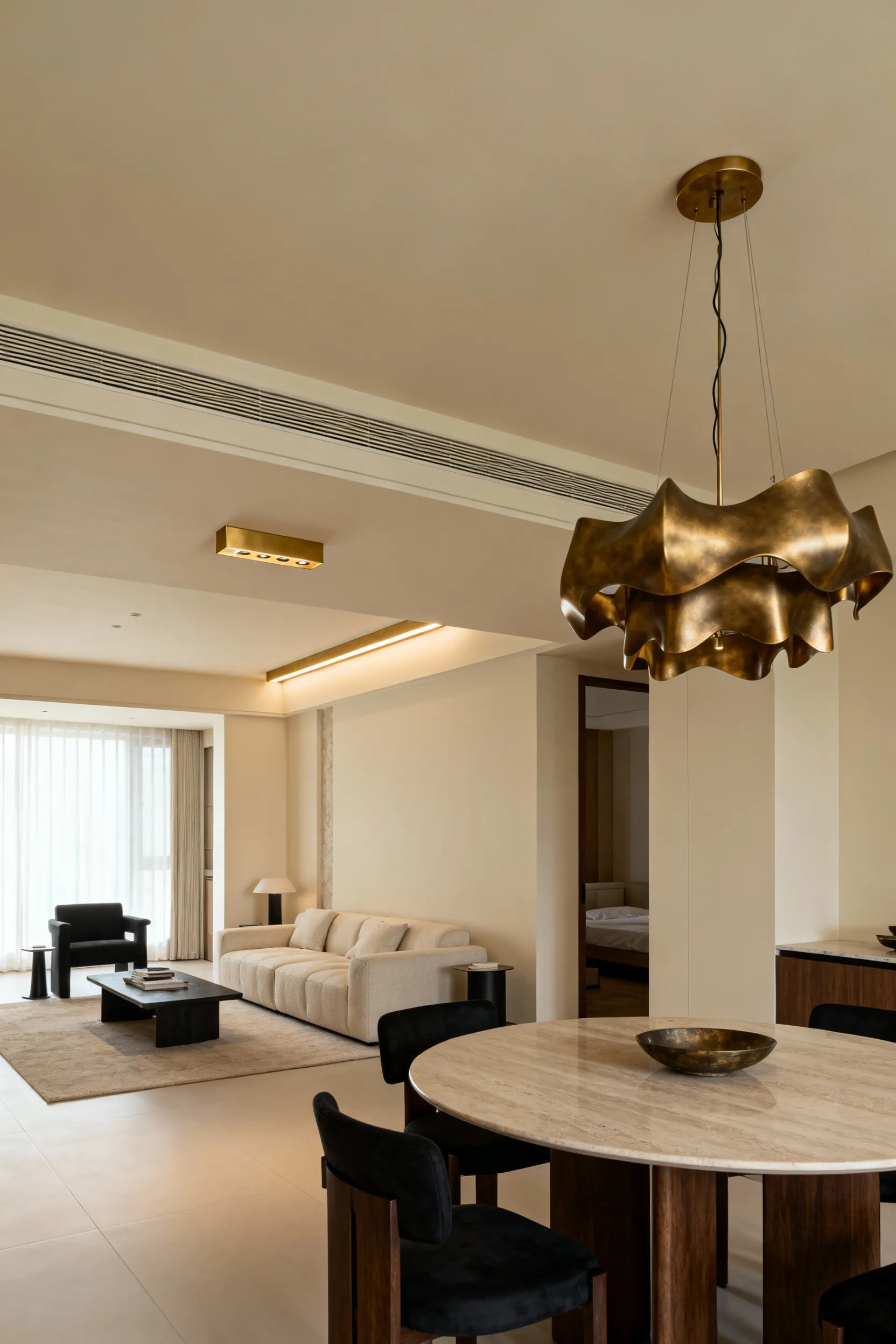 An elegant open-concept living and dining area with harmonized brushed brass pendant lights over the dining table and a matching linear fixture in the living area, showcasing cohesive luminaire styles and finishes.