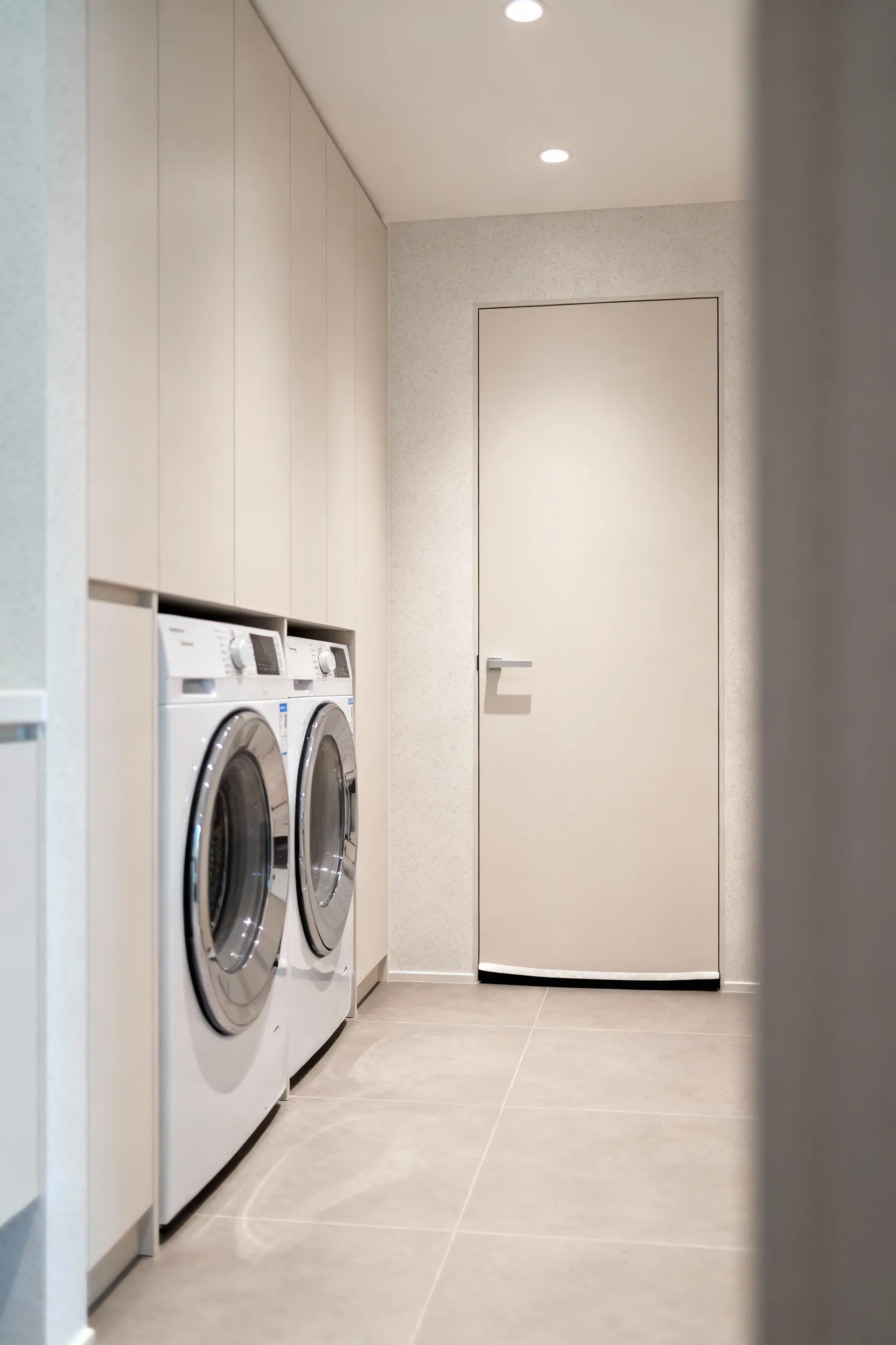 Modern mudroom laundry room designed with noise reduction in mind, featuring sleek, quiet appliances, a sound-isolating solid-core door, and acoustic wall treatments, captured in a bright, clean aesthetic.