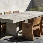 A minimalist patio design featuring a raw concrete table and weathered wood seating to showcase the philosophy of materiality and texture.