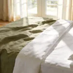 High-quality interior photo of a cozy bedroom featuring the textural contrast between soft rumpled linen and crisp structured percale bedding.