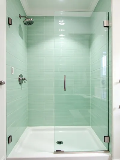 Modern coastal bathroom shower featuring seafoam green subway tile walls, brushed nickel fixtures, glass door, and white shower pan, illuminated by soft, diffused lighting.