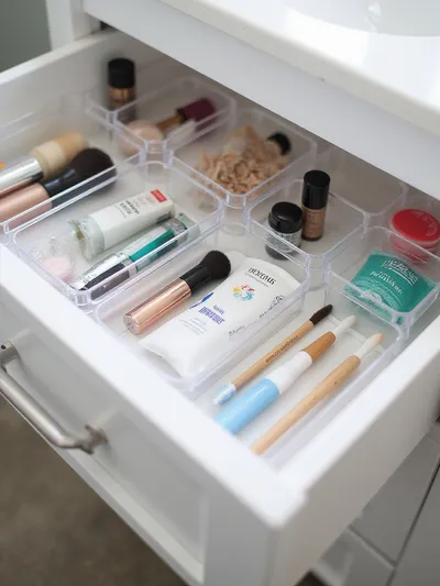 Organized bathroom drawer with clear acrylic dividers filled with small items.