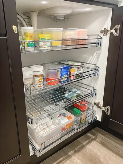 Organized under-sink cabinet with multi-tier sliding organizers, showcasing cleaning supplies.