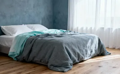 A serene bedroom featuring gray-blue walls and pale aqua linen bedding, designed to anchor the spirit and promote deep relaxation through cool, muted colors.