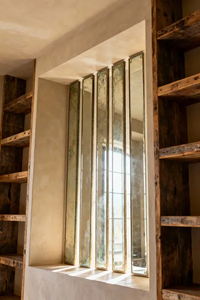 Vertical antiqued mirror panels in a farmhouse bathroom recessed niche, reflecting diffused natural light and reclaimed wood shelves, creating an illusion of expanded space.