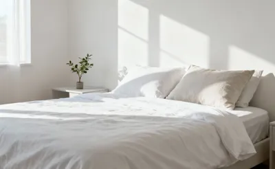 A serene, minimalist bedroom with clean lines and decluttered surfaces, illuminated by soft natural light. Represents the calm achieved through bedroom decluttering.