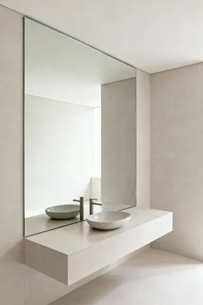 Modern bathroom with large frameless mirror reflecting an expansive space, showcasing strategic mirror placement for volume amplification and increased brightness.
