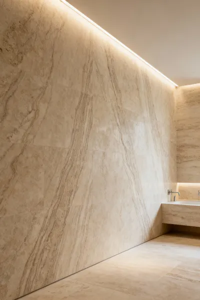 Luxury bathroom featuring floor-to-ceiling book-matched travertine slabs, demonstrating anthropometric design principles for human scale and perception. Seamless wall embellishments create a visually expansive and serene atmosphere. Minimalist, modern aesthetic with soft lighting.
