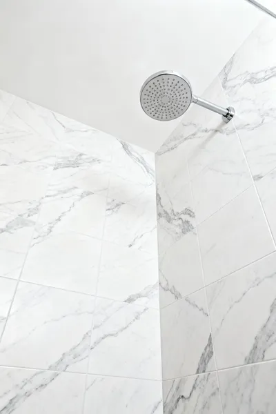 Luxury bathroom shower wall featuring large-format, book-matched porcelain stoneware tiles that replicate Statuario marble, showcasing seamless design and minimal grout lines, enhancing a modern bathscape.