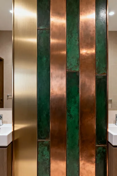 Close-up of a luxurious bathroom wall featuring stratified metallic panels: brushed champagne-anodized aluminum and deep green patinated copper, showcasing reflective depth.
