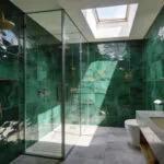 A luxurious bathroom featuring emerald green Zellige wall tiles that catch and scatter natural sunlight to create a shimmering effect.